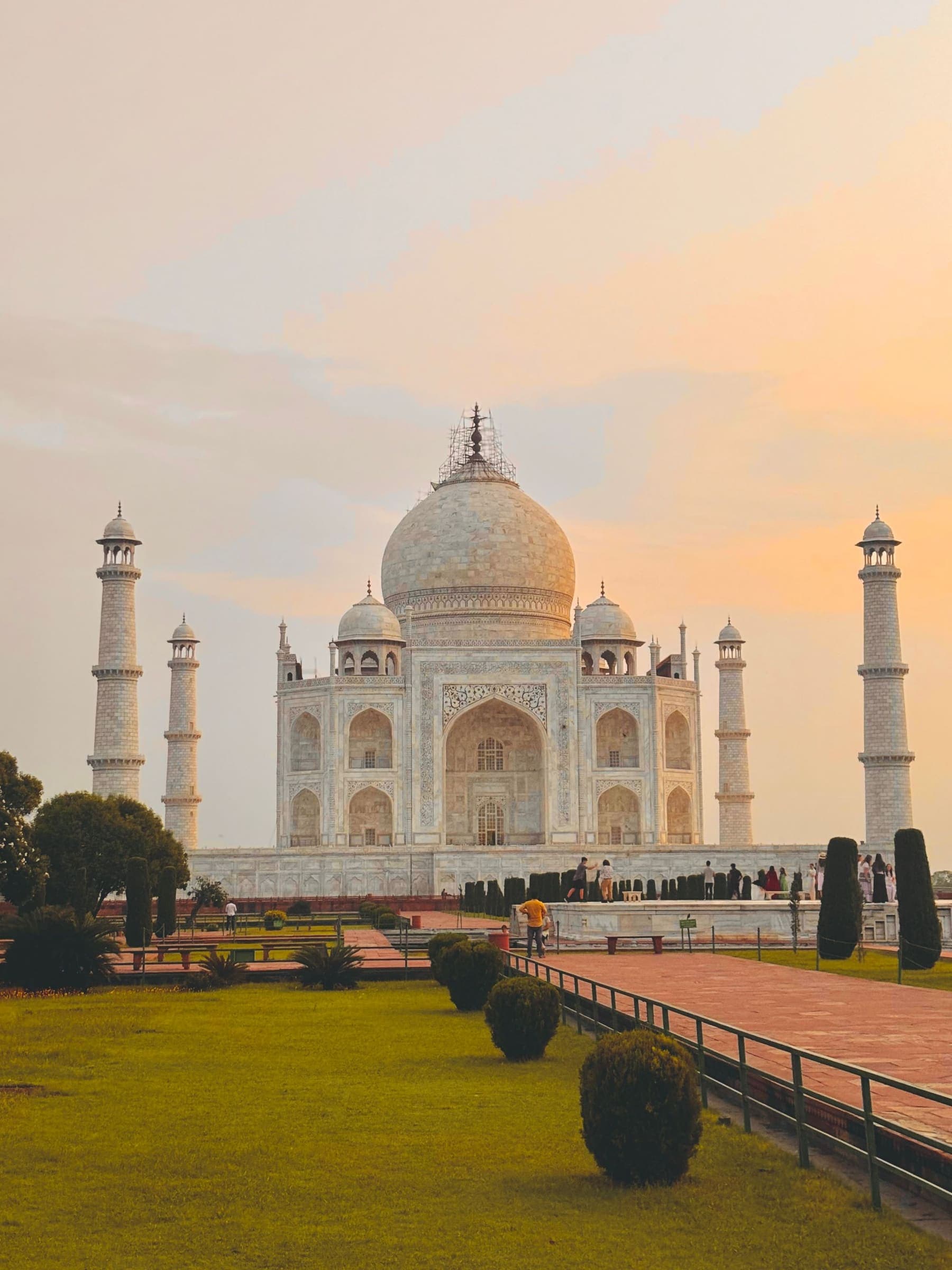The Taj Mahal and its four minarets under a pink and orange early-morning sky, seen from the gardens